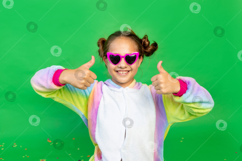 Скачать маленькая девочка на зеленом фоне в ярком костюме и очках показывает поднятые вверх большие пальцы. Место для текста. Концепция праздника, Дня рождения и распродаж фотосток Ozero
