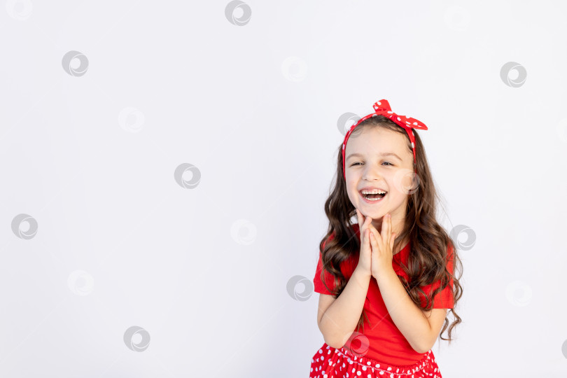 Скачать Симпатичная маленькая девочка в красном платье на белом изолированном фоне сложила руки на щеках. Место для текста. Маленькая девочка празднует день рождения, концепция праздника и распродажи фотосток Ozero