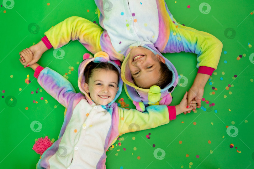 Скачать маленькие девочки в ярких костюмах лежат на зеленом изолированном фоне с серпантином в ярких костюмах единорогов. Концепция праздника, Дня рождения и распродаж фотосток Ozero