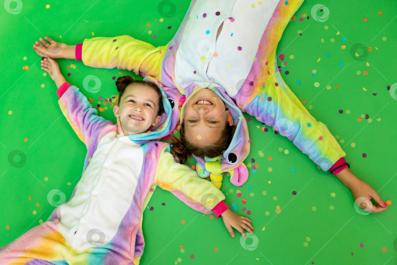 Скачать маленькие девочки в ярких костюмах лежат на зеленом изолированном фоне с серпантином в ярких костюмах единорогов. Концепция праздника, Дня рождения и распродаж фотосток Ozero