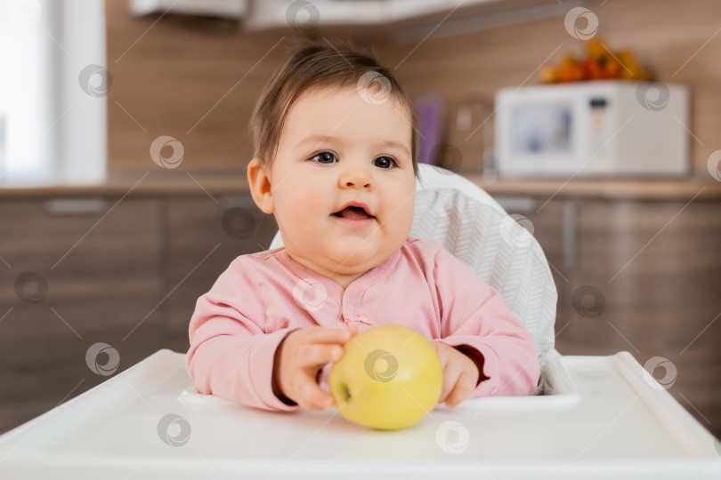 Скачать Маленькая девочка сидит на детском стульчике на кухне и ест овощи фотосток Ozero