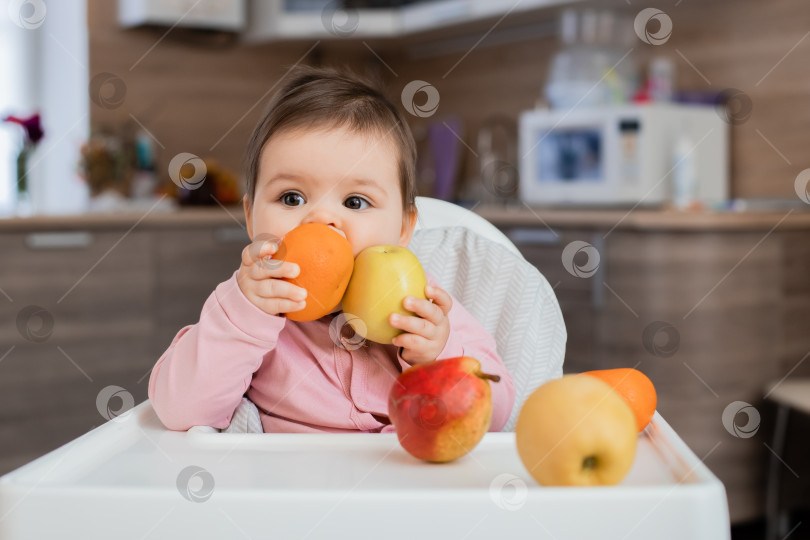 Скачать Маленькая девочка сидит на детском стульчике на кухне и ест овощи фотосток Ozero