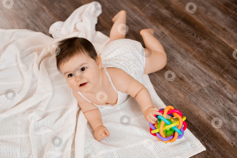 Скачать Маленькая девочка лежит на деревянном полу и играет с развивающей игрушкой фотосток Ozero