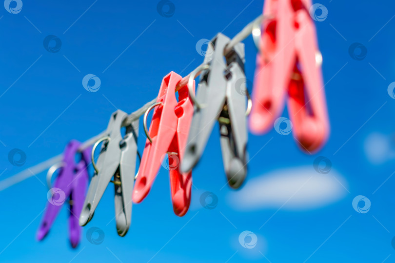 Скачать Разноцветные прищепки висят на бельевой веревке, леске для одежды и постельного белья на размытом фоне голубого неба в солнечный день. фотосток Ozero