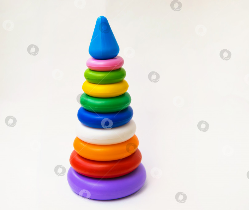 Скачать Детская пластиковая игрушка, пирамидка из цветных колец на белом фоне. Развитие и воспитание ребенка. фотосток Ozero