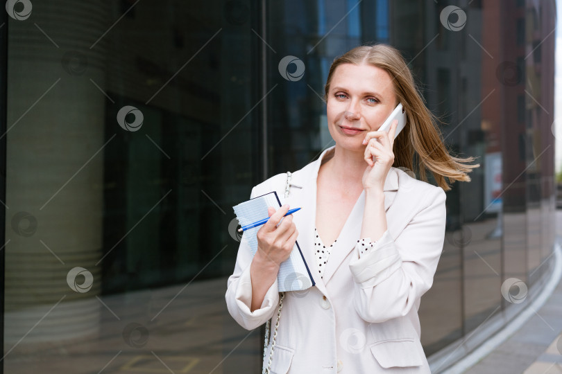 Скачать Красивая светловолосая девушка держит в руках смартфон и блокнот. фотосток Ozero