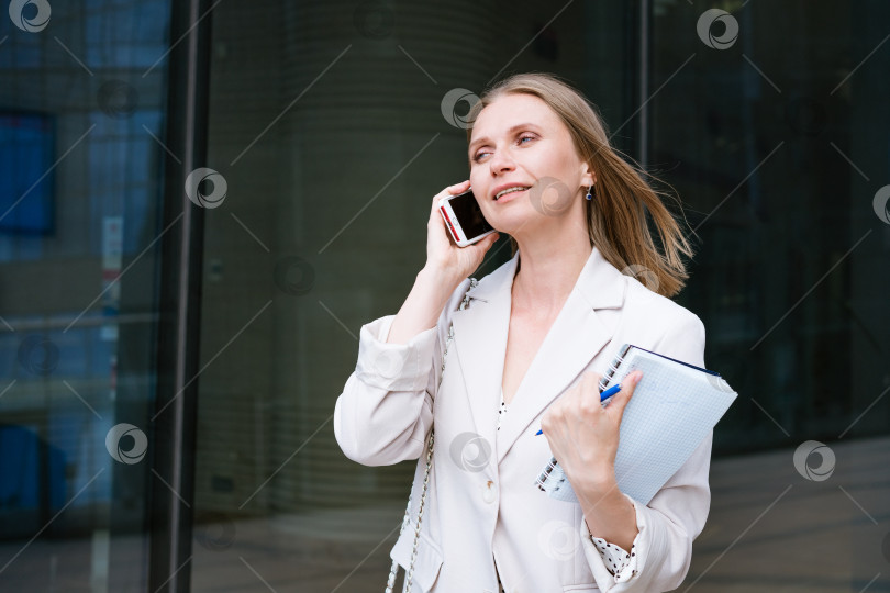 Скачать Успешная деловая женщина или бизнесвумен, делающая заметки и разговаривающая по мобильному телефону во время прогулки на свежем воздухе. Деловая женщина фотосток Ozero