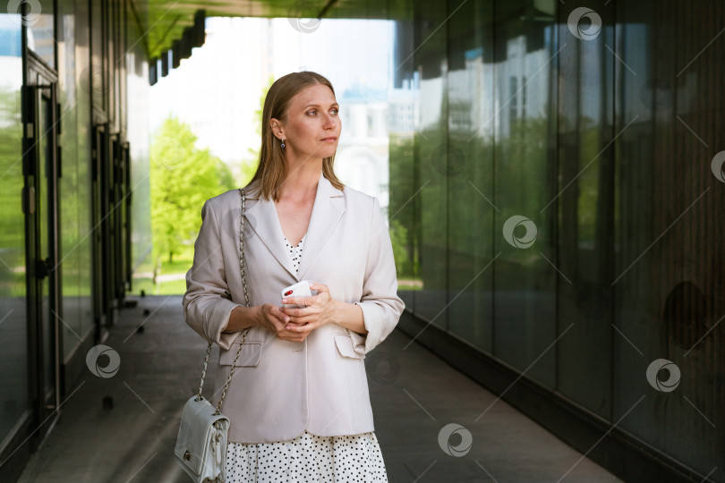 Скачать Улыбающаяся женщина в повседневной одежде стоит у входа в офис. Деловая женщина фотосток Ozero