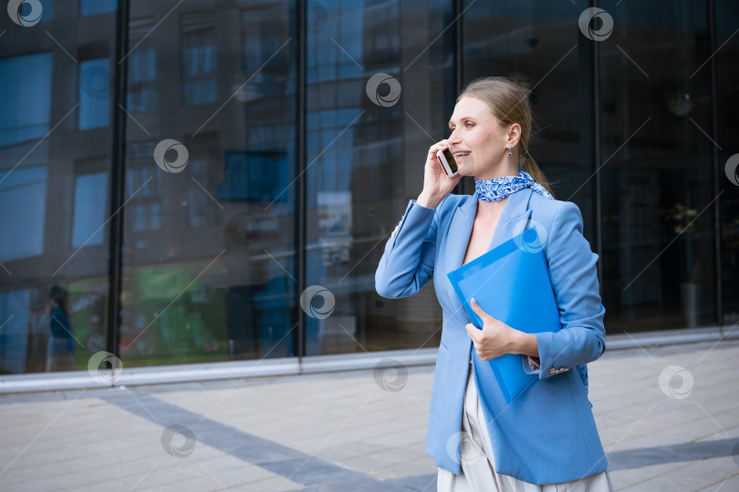 Скачать деловая женщина в синем разговаривает по телефону с папкой в руке фотосток Ozero