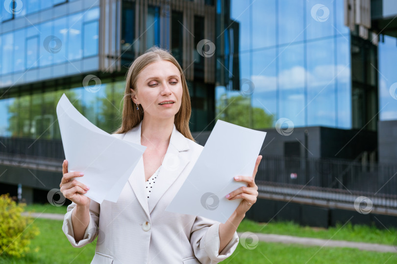 Скачать Деловая женщина, успешный исполнительный директор, читает бумажные документы в легкой куртке, стоя на улице возле фотосток Ozero