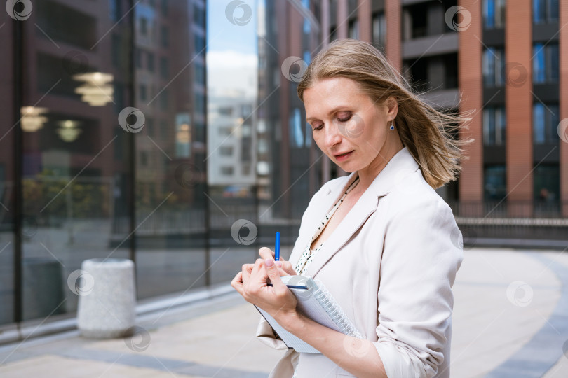 Скачать Деловая женщина в светлом жакете стоит и пишет что-то рядом с бизнесом фотосток Ozero