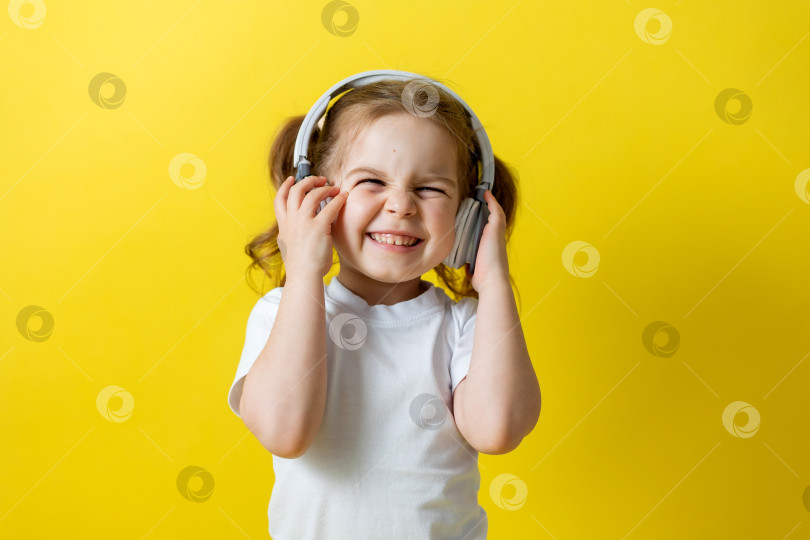Скачать маленькая девочка в белой футболке слушает музыку в наушниках на желтом фоне, улыбаясь. пространство для текста фотосток Ozero
