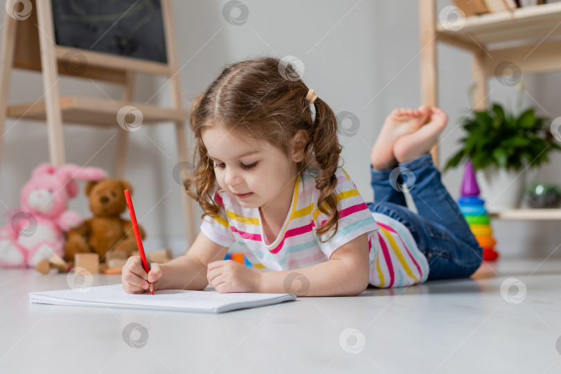 Скачать милая маленькая девочка лежит на деревянном полу и рисует в детской комнате фотосток Ozero