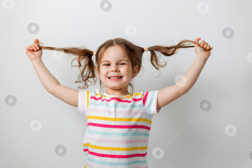 Скачать портрет милой девушки на светлом фоне, играющей со своими волосами фотосток Ozero