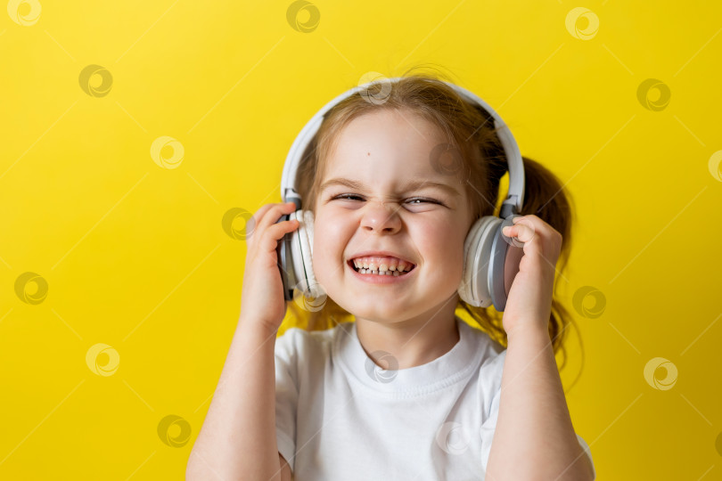Скачать маленькая девочка в белой футболке слушает музыку в наушниках на желтом фоне, улыбаясь. пространство для текста фотосток Ozero
