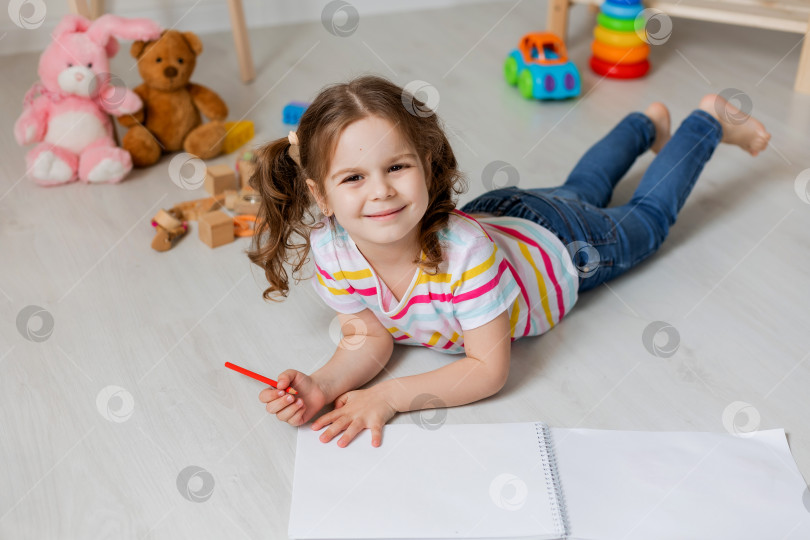 Скачать милая маленькая девочка лежит на деревянном полу и рисует в детской комнате фотосток Ozero