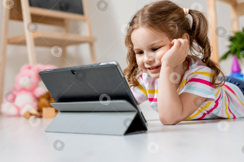 Скачать милая маленькая девочка лежит на деревянном полу в детской комнате и играет с планшетом фотосток Ozero