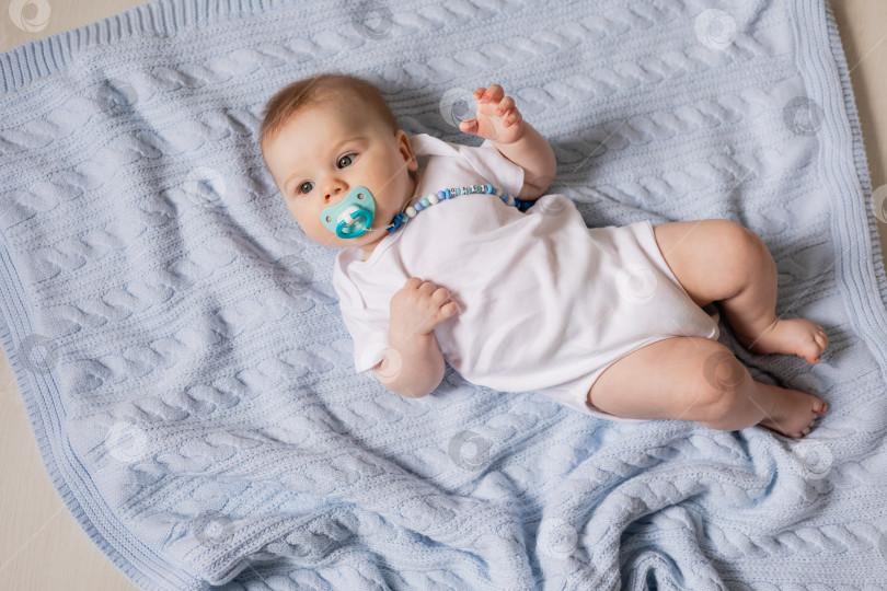 Скачать портрет ребенка 3 месяцев, лежащего на синем вязаном одеяльце, синяя соска, вид сверху фотосток Ozero