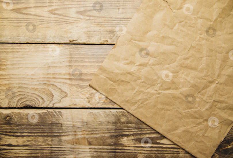 Скачать Крафт-бумага на деревянном фоне.Мятая бумага, шероховатая поверхность. фотосток Ozero