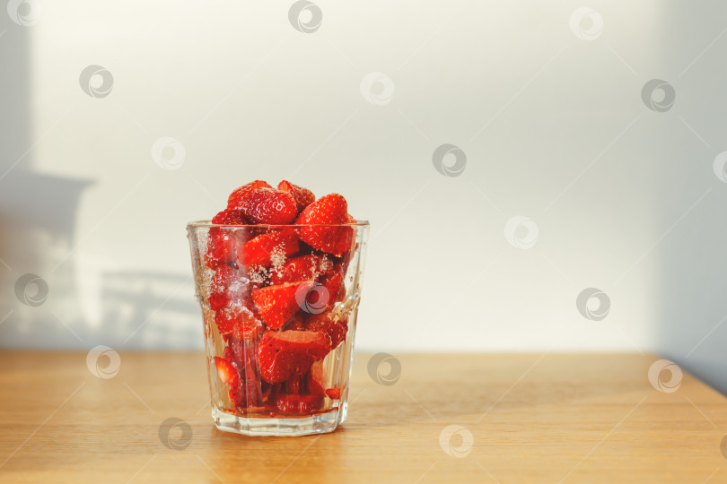 Скачать Кусочки свежих спелых ягод клубники в стакане на кухонном столе. фотосток Ozero