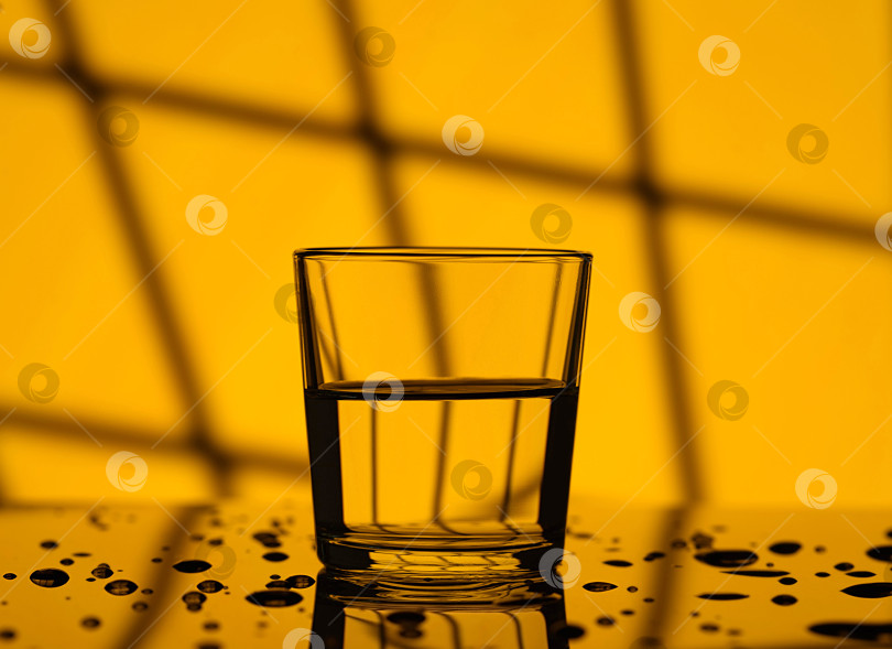Скачать Утром налейте воду в стакан в селективном режиме. Желтый фон оконной решетки. фотосток Ozero