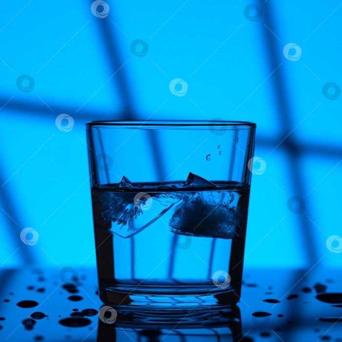 Скачать Вечером налейте воду в стакан со льдом в селективной концентрации. Синий фон оконной решетки. фотосток Ozero
