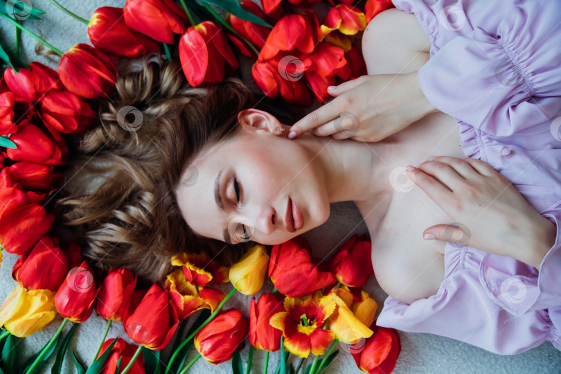 Скачать Молодая женщина лежит на полу среди красных тюльпанов. Концепция 8 марта, Дня святого Валентина. Весенний портрет женщины. фотосток Ozero