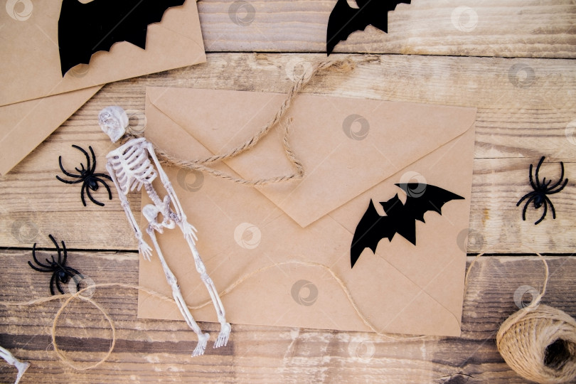 Скачать Конверт из крафт-бумаги и войлочные летучие мыши, скелеты, пауки вокруг на деревянном фоне. фотосток Ozero