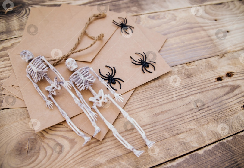 Скачать Конверт из крафт-бумаги и войлочные скелеты, пауки вокруг на деревянном фоне. Декор на Хэллоуин. фотосток Ozero