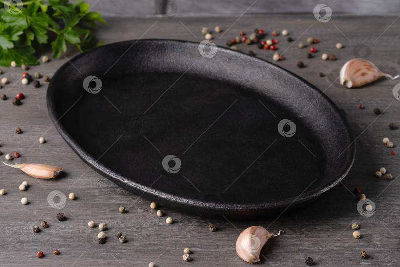 Скачать Пустая черная тарелка на сером фоне со специями и зеленью. фотосток Ozero