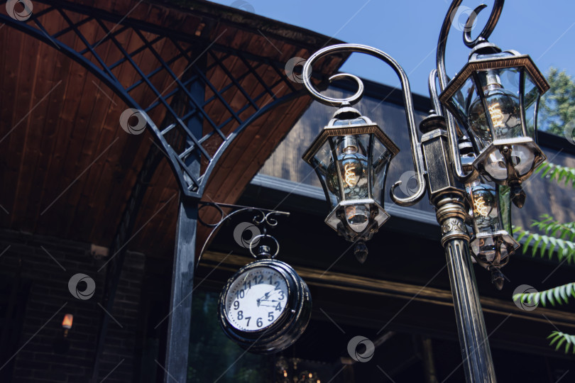Скачать Декоративный фонарный столб из кованого железа и большие часы у входа фотосток Ozero