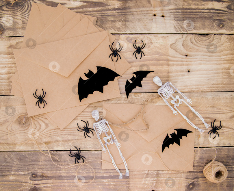 Скачать Конверт из крафт-бумаги и войлочные летучие мыши, скелеты, пауки вокруг на деревянном фоне. фотосток Ozero