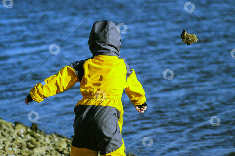 Скачать Ребенок бросает камень в воду. Камень взлетает в воздух. фотосток Ozero