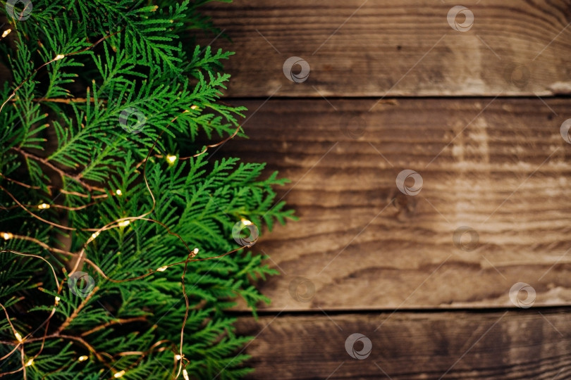 Скачать Фон рождественских огней из зеленых ветвей туи. Праздничная блестящая гирлянда и ветки на поверхности деревянных досок. фотосток Ozero