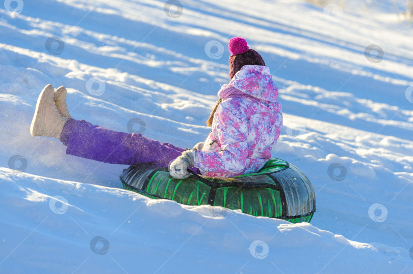 Скачать Молодая женщина катается на тюбингах с холма по снегу зимой. Зимнее развлечение. Снежная забава. фотосток Ozero