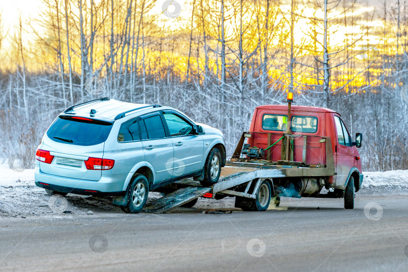 Скачать Погрузка сломанного автомобиля на эвакуатор. Поврежденный в результате аварии автомобиль на зимнем шоссе. фотосток Ozero