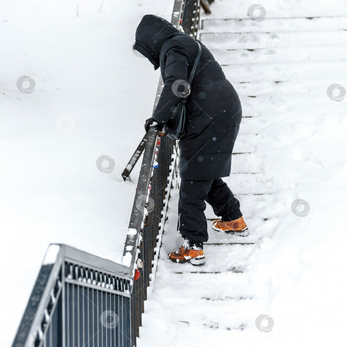 Скачать Женщина спускается или поднимается по лестнице в снегу, держась руками за перила, чтобы не упасть.Заснеженные лестницы, риск падения на скользких ступенях зимой. фотосток Ozero
