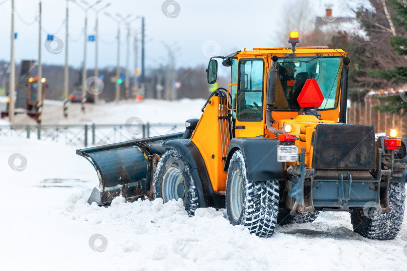 Скачать Снегоочиститель, трактор в выборочном фокусе убирают снег на проезжей части улицы в снежную бурю. Вид сзади. Служба уборки снега, работающая зимой. фотосток Ozero