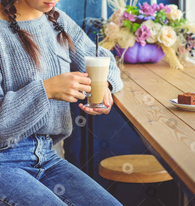 Скачать Молодая девушка сидит в кафе и держит в руках чашку кофе. Красивая стеклянная кружка с соломинкой. фотосток Ozero
