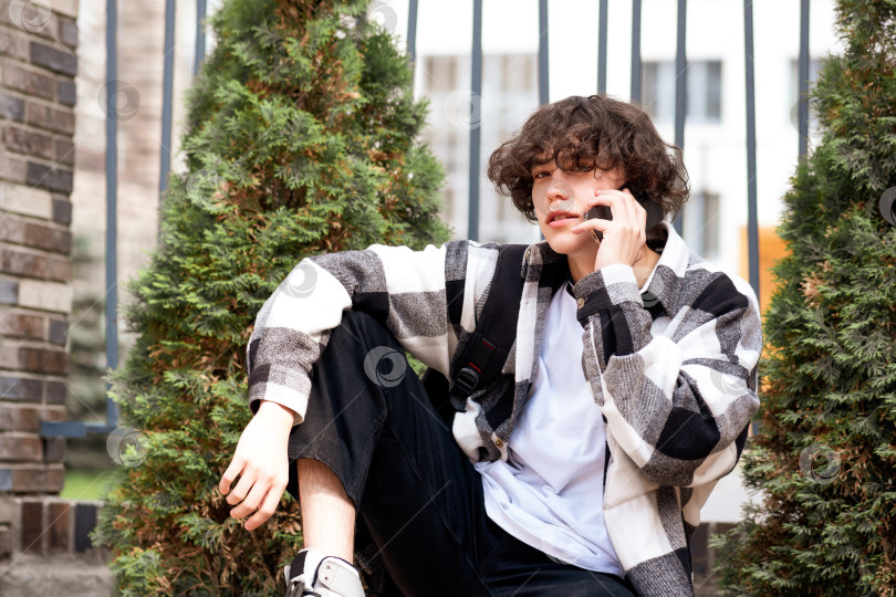 Скачать молодой человек разговаривает по телефону, сидя на скамейке в центре города. фотосток Ozero