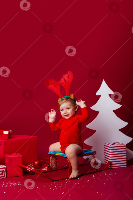 Скачать Симпатичный малыш с оленьими рогами на голове сидит на санках с рождественскими подарками. концепция родства, пространство для текста фотосток Ozero