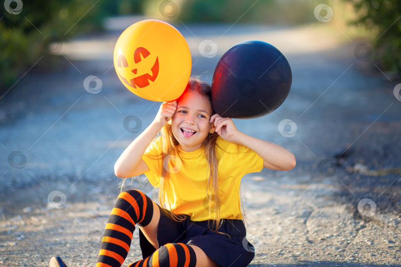 Скачать Веселая девушка в костюме для Хэллоуина сидит на дороге и корчит рожи воздушными шариками фотосток Ozero