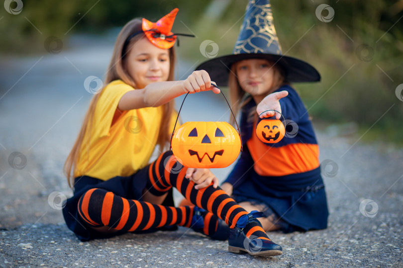 Скачать Две девушки в костюмах на Хэллоуин сидят на дороге и показывают конфеты в виде веселых тыкв фотосток Ozero