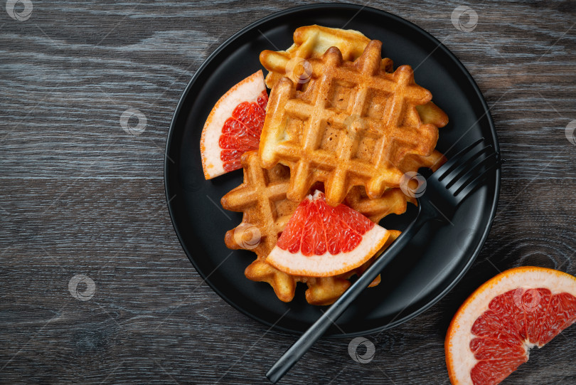 Скачать Вафли и грейпфрут в черной тарелке на деревянном столе. фотосток Ozero