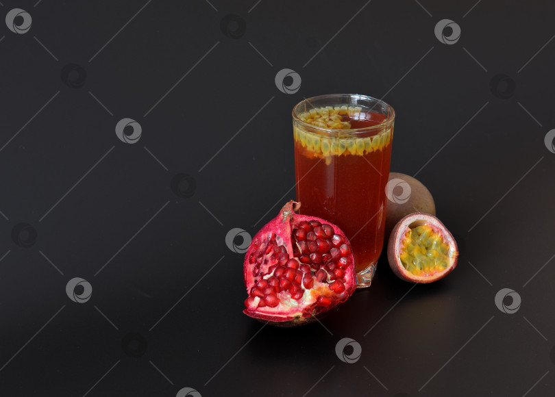 Скачать Высокий стакан фруктового сока с косточками на черном фоне, рядом с разломанным плодом граната и кусочками спелой маракуйи. фотосток Ozero