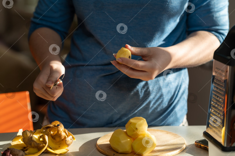 Скачать Крупный план женских рук, чистящих картошку над кухонным столом. фотосток Ozero