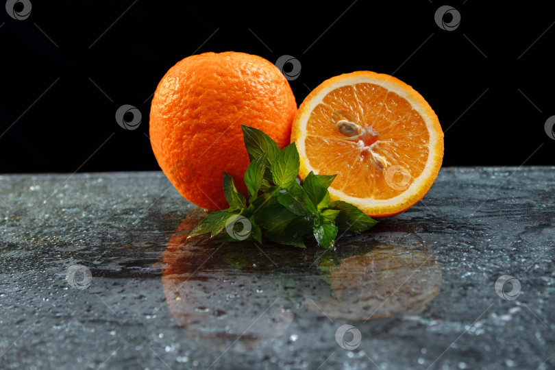 Скачать Апельсин, лежащий на стеклянном столе, с каплями воды и пучком мяты на черном фоне фотосток Ozero