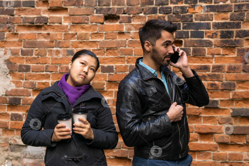 Скачать молодой человек разговаривает по телефону, девушка скучает с двумя бумажными стаканчиками фотосток Ozero