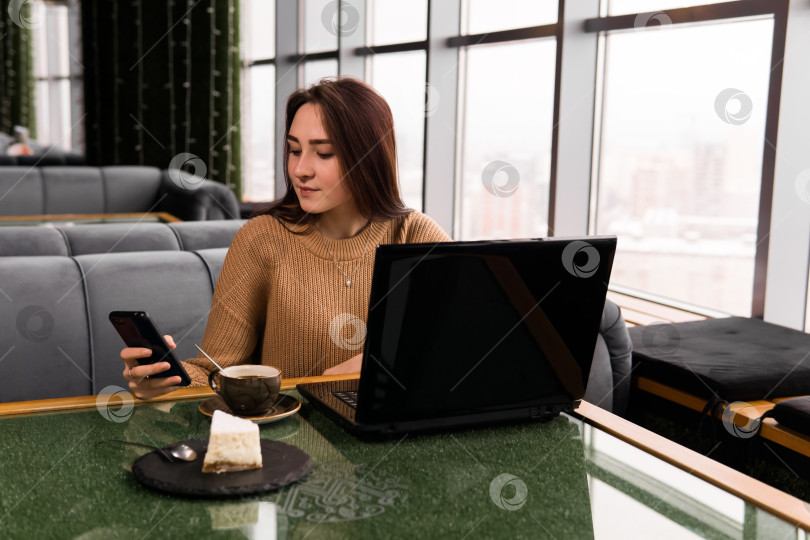Скачать молодая женщина работает с ноутбуком и смартфоном в кофейне фотосток Ozero