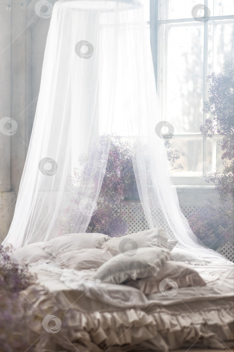 Скачать Кровать в светлой спальне в пастельных тонах в стиле бохо, трендовом цвете 2023 года. Комната украшена сиреневыми и розовыми цветами гипсофилы, винтажный декор в комнате в стиле ретро лофт. фотосток Ozero